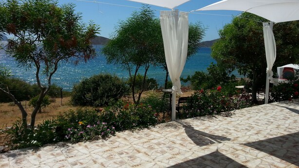 Una terraza con vista al mar, cubierta por toldos blancos y rodeada de follaje.