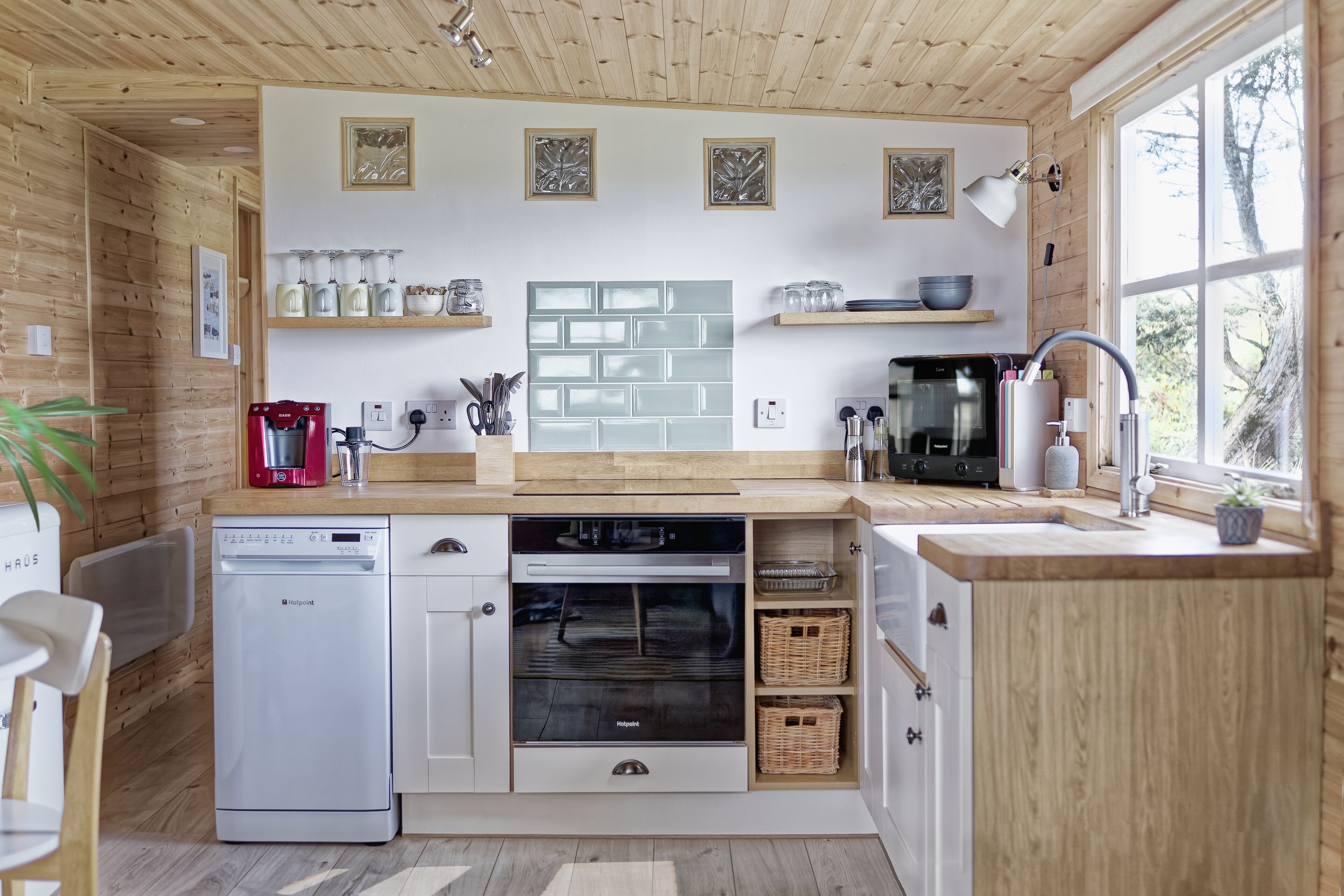 Une cuisine moderne avec des meubles en bois, un four encastré, une machine à café et une fenêtre qui laisse entrer la lumière naturelle.