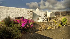 A white building with stone accents, a small tower, and a paved area with pink flowers. - Casa de Los Olivos (Macher)