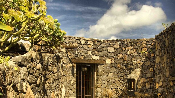 A stone-walled courtyard with a tiled floor, a metal gate, and a small window. - Casa de Los Olivos (Macher)