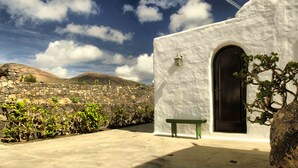A white building with a stone wall, a bench, and a mountain in the background. - Casa de Los Olivos (Macher)