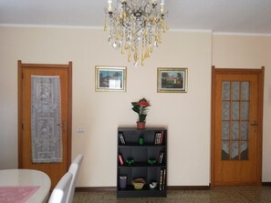 Une pièce avec un lustre, deux tableaux encadrés au mur, une bibliothèque contenant divers objets et deux portes.