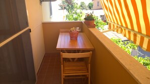 En lille balkon med et træbord og en stol, en potteplante og udsigt over et boligområde.