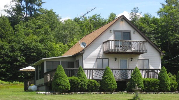 A two-story house with a balcony, surrounded by a well-maintained lawn and trees.