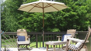 A wooden deck with a cushioned chair and a lounge chair, a potted plant, and a large umbrella.