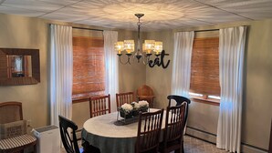 A dining room with a round table, six wooden chairs, a central chandelier, and a wall-mounted mirror.