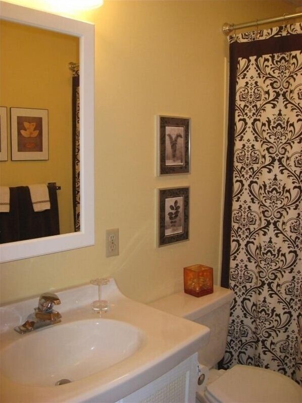 A bathroom with a sink, mirror, and toilet. There are three framed pictures on the wall.