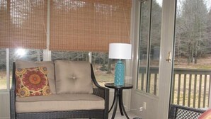 A wicker sofa with a cushion and a patterned pillow, a small round table with a lamp, and a wicker chair.