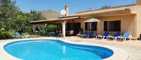 A swimming pool with blue water, surrounded by lounge chairs and a covered patio area.