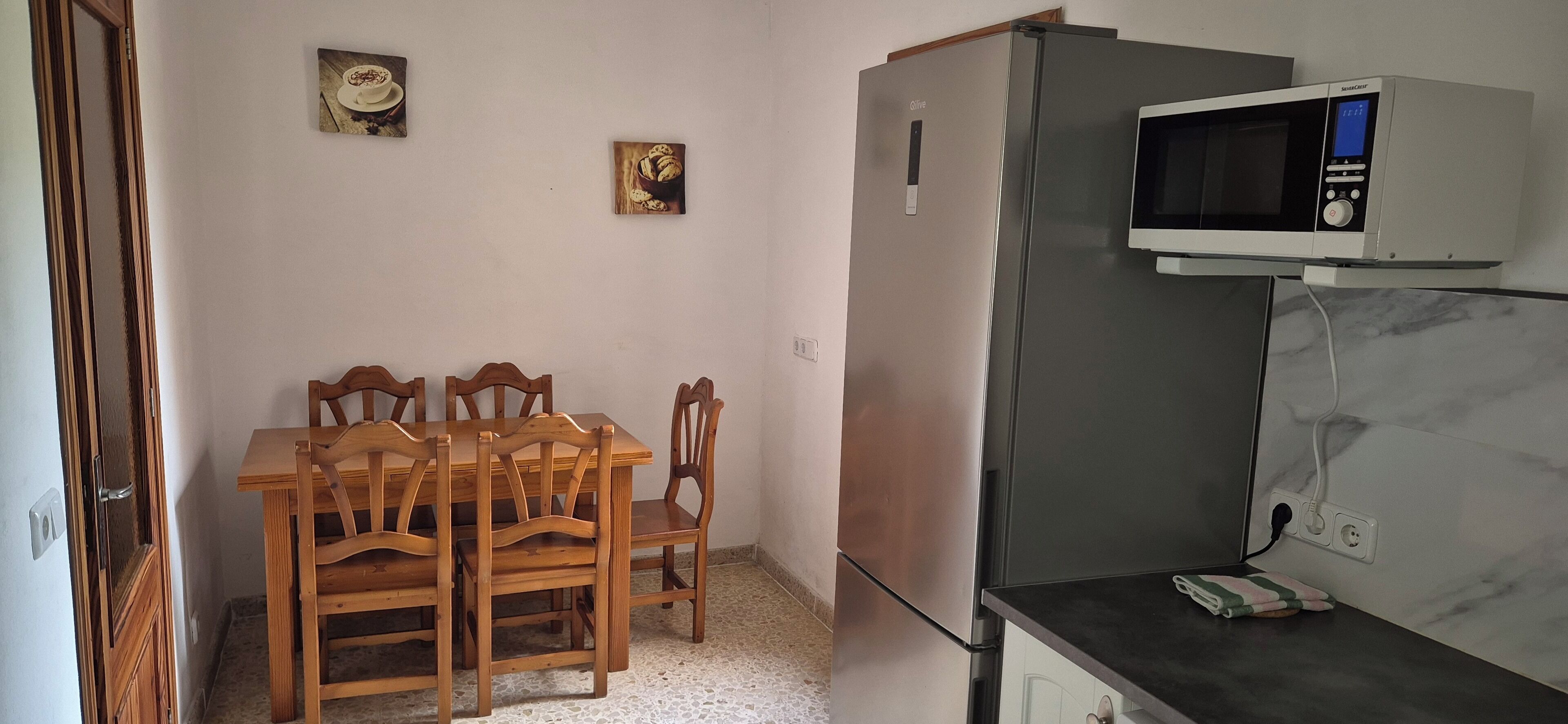 Eine kleine Küche mit Kühlschrank, Mikrowelle und einem Esstisch mit Stühlen.