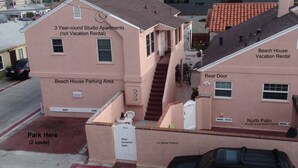 A pink two-story building with a rear door, a rear entrance gate, and a parking area marked "Park Here (2 spots)".