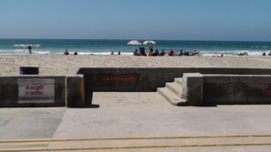 A beach with a concrete barrier, a warning sign, and people relaxing under umbrellas.