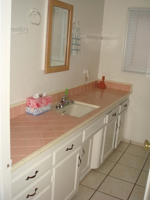 A kitchen with a sink, countertop, cabinets, and a window with blinds.
