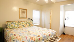 A bedroom with a bed, a framed picture on the wall, a door, and a window with blinds.