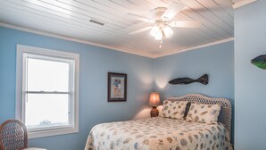 Ein Schlafzimmer mit Bett, Sessel, Fenster und Deckenventilator, inklusive Wanddekorationen.