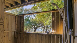 Eine Holzhütte mit einer Holzterrasse, einer Dusche und Blick auf Bäume und den Strand.