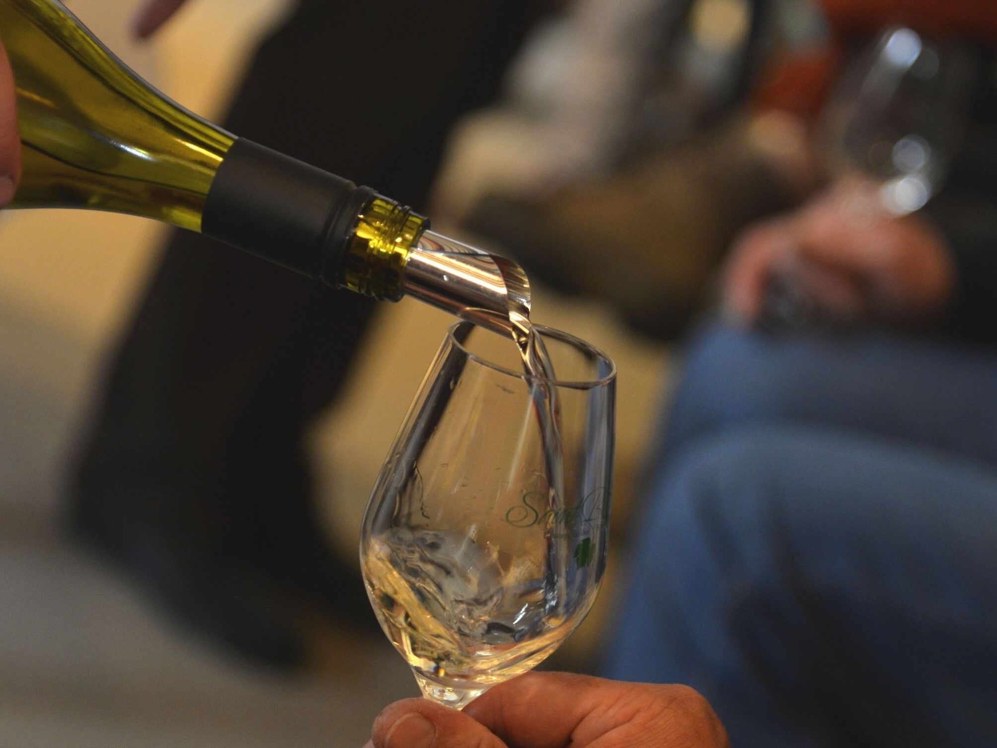 Een hand die een wijnglas vasthoudt, terwijl wijn uit een fles wordt geschonken.