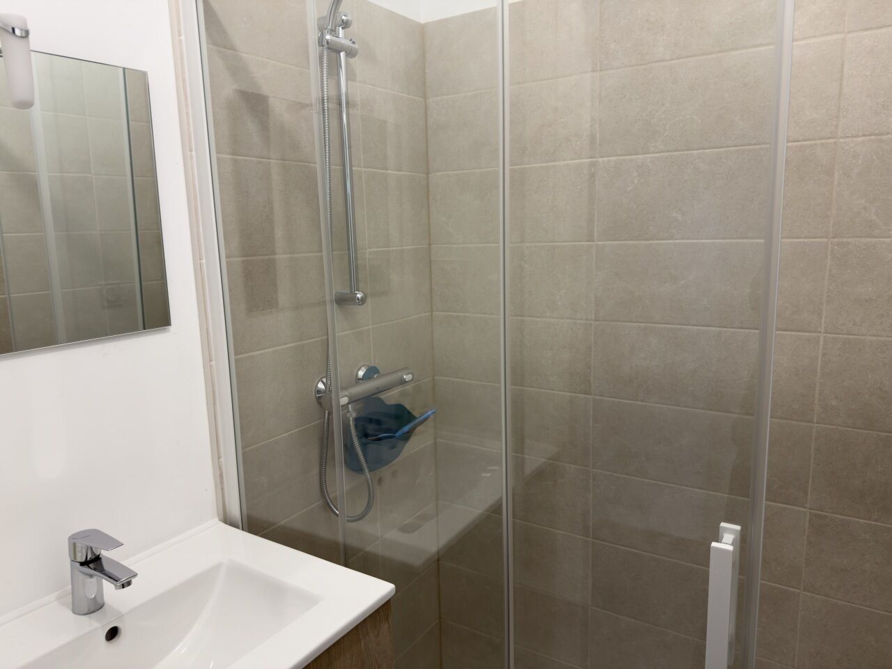 A bathroom with a glass shower enclosure, a white sink, and a mirror.