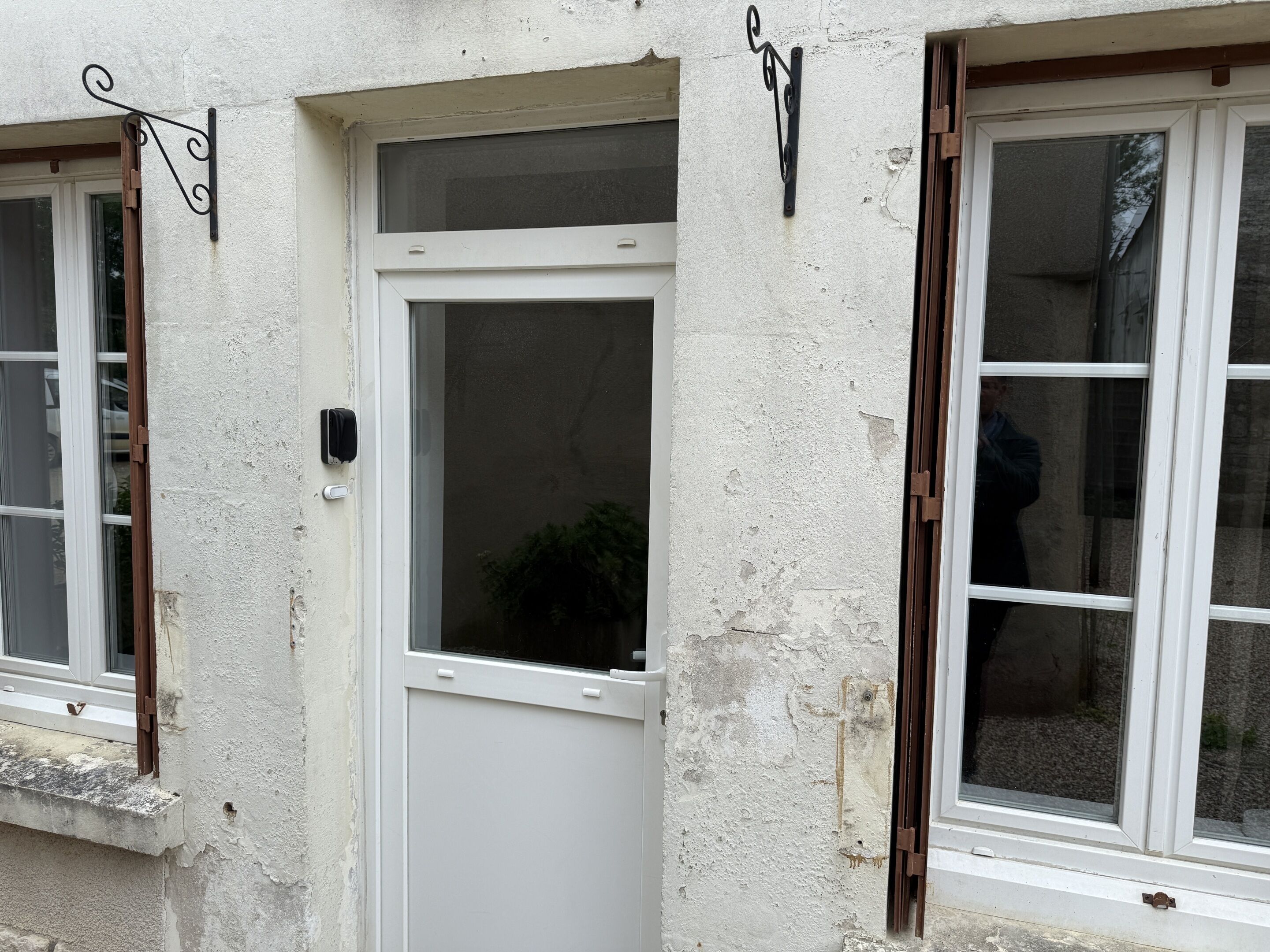 A white door with a window, a small plant visible through the window, and a metal decorative bracket on the wall.