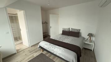 A bedroom with a bed, a nightstand, a lamp, a coat rack, and a door leading to a bathroom.