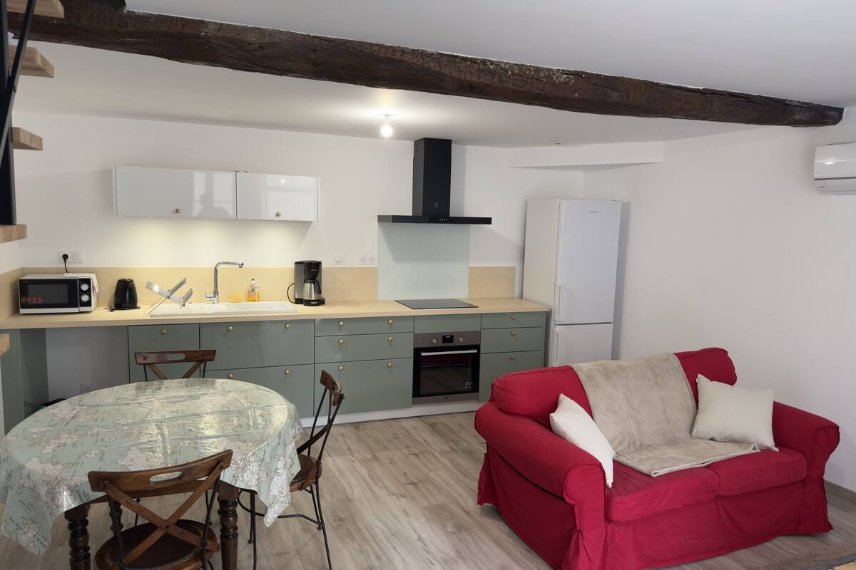 Eine kleine Küche mit Mikrowelle, Kaffeemaschine und Kühlschrank. Es gibt einen Esstisch mit Stühlen und ein rotes Sofa mit Kissen.