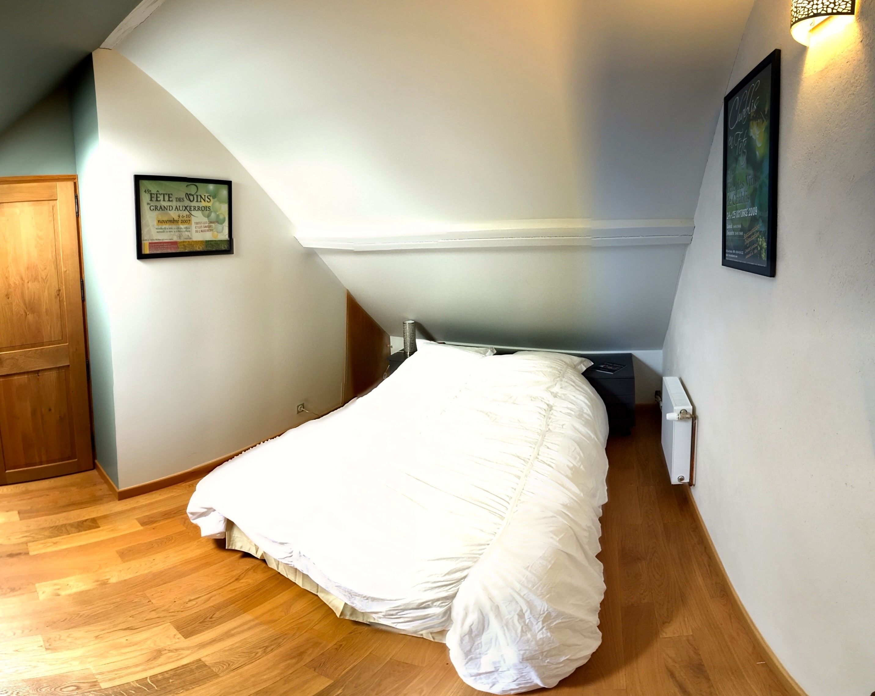 Un dormitorio con cama, suelo de madera, un radiador y un cartel enmarcado en la pared.
