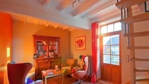 A cozy room with a wooden bookshelf, a red armchair, a small table, and a window with curtains. - Les Temps Perdus (Prehy)