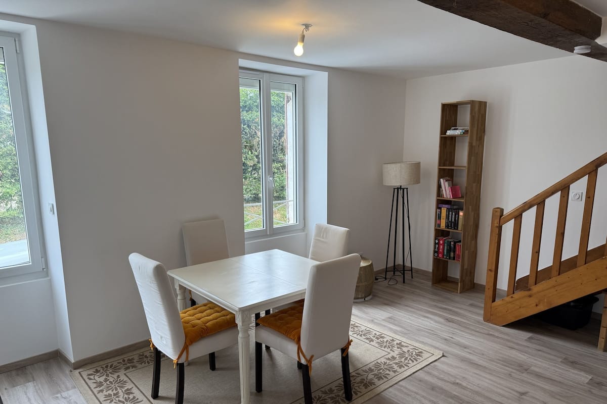 Ein Zimmer mit weißem Tisch und Stühlen, einem Bücherregal, einer Lampe und einer Treppe.