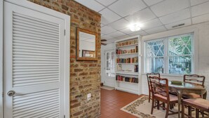 A room with a brick wall, a white door, a bookshelf, a dining table with chairs, and a window with blinds. - Intimate Getaway for Two, Steps from Forsyth Park by Lucky Savannah (Savannah)