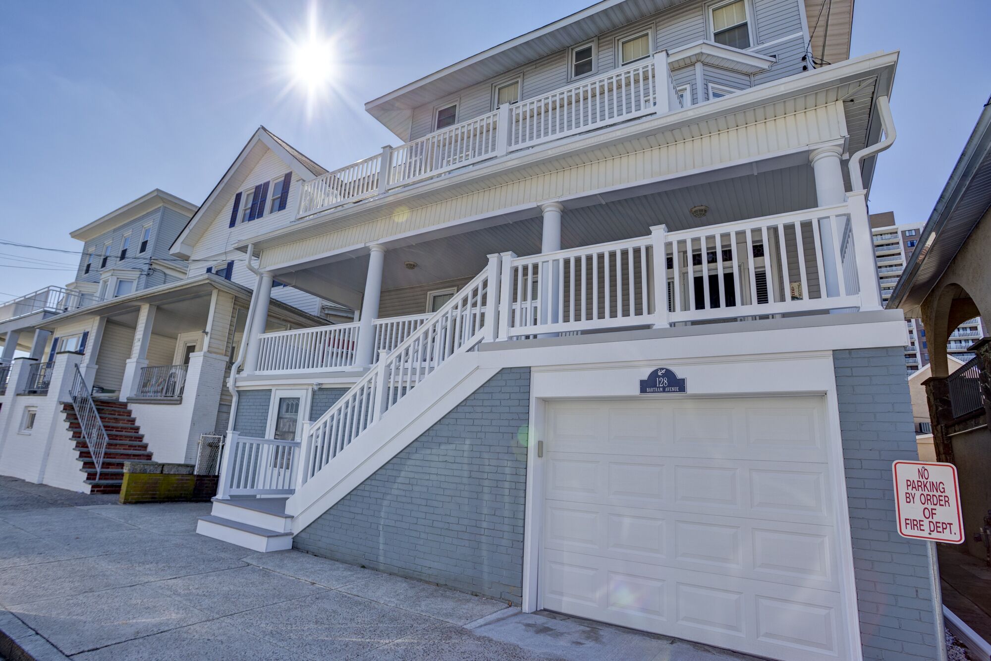 A multi-story residential building with a prominent front staircase, a garage, and a no parking sign.