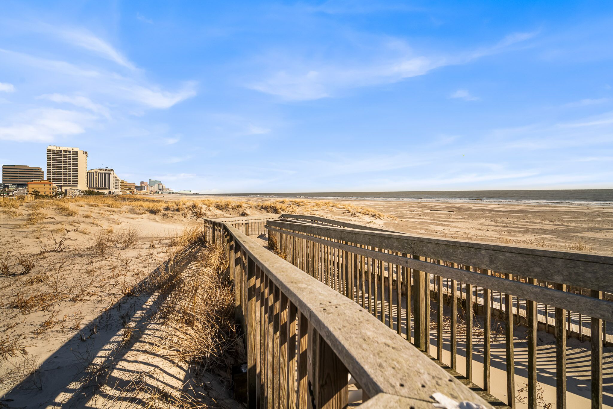 A wooden boardwalk along a beach with sandy dunes and a clear sky.