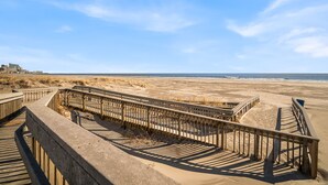 A wooden boardwalk leading to a sandy beach with a clear sky.