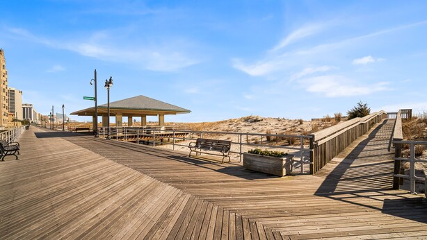 A wooden boardwalk leading to a covered pavilion with benches and a planter.