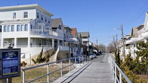 A coastal street lined with multi-story buildings, featuring balconies and a boardwalk with railings.