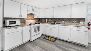 A modern kitchen with white cabinets, a microwave, stove, and a brick backsplash.