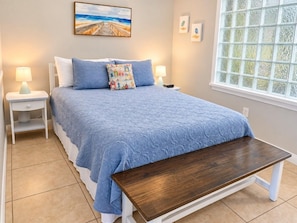 Une chambre à coucher comprenant un lit, des tables de chevet, un banc, une fenêtre à vitre dépolie et des œuvres d’art murales.