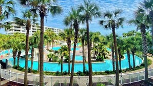 Un complexe hôtelier doté de plusieurs piscines, entouré de palmiers et délimité par une clôture blanche.