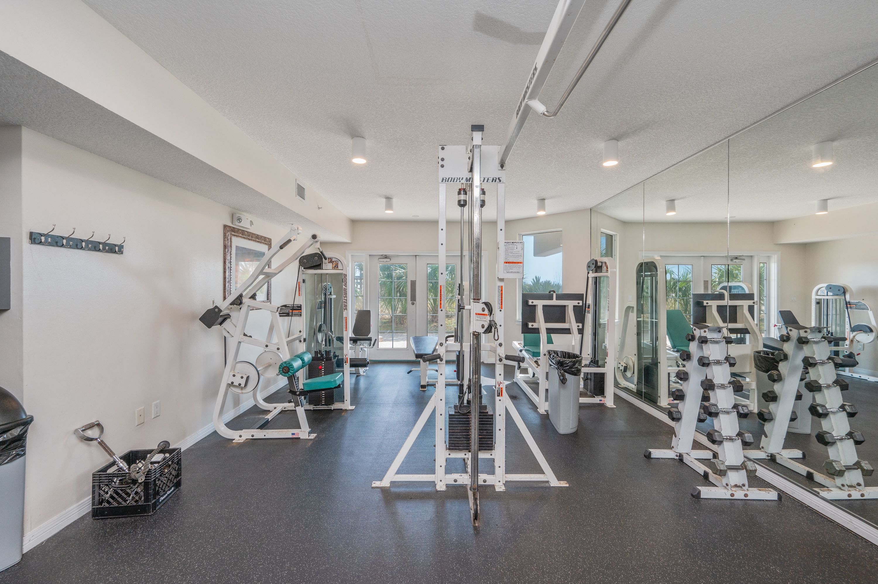 A gym with various exercise equipment, a mirror wall, and a door leading outside.