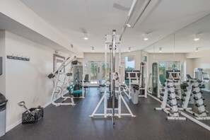 Een sportschool met diverse fitnessapparaten, een spiegelwand en een deur naar buiten.