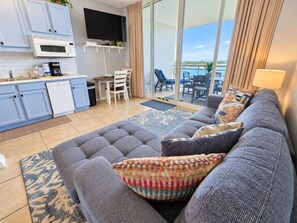 A modern living room with a grey sofa, a flat-screen TV, and a balcony with a pool view.