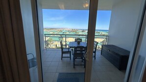 Un balcon avec une table et des chaises, un petit canapé et une vue sur une zone côtière avec des bâtiments et un pont.