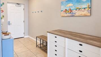 A hallway with a white door, a small table, a bench, and a wall-mounted cabinet.
