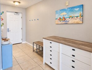 A hallway with a white door, a small table, a bench, and a wall-mounted cabinet.