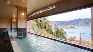 A spa area with a large indoor pool, wooden ceiling, and a view of mountains and trees. - Rakuyu (Fujikawaguchiko)