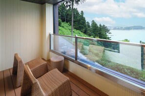 A balcony with wicker furniture, a glass railing, and a view of a lake and greenery.
