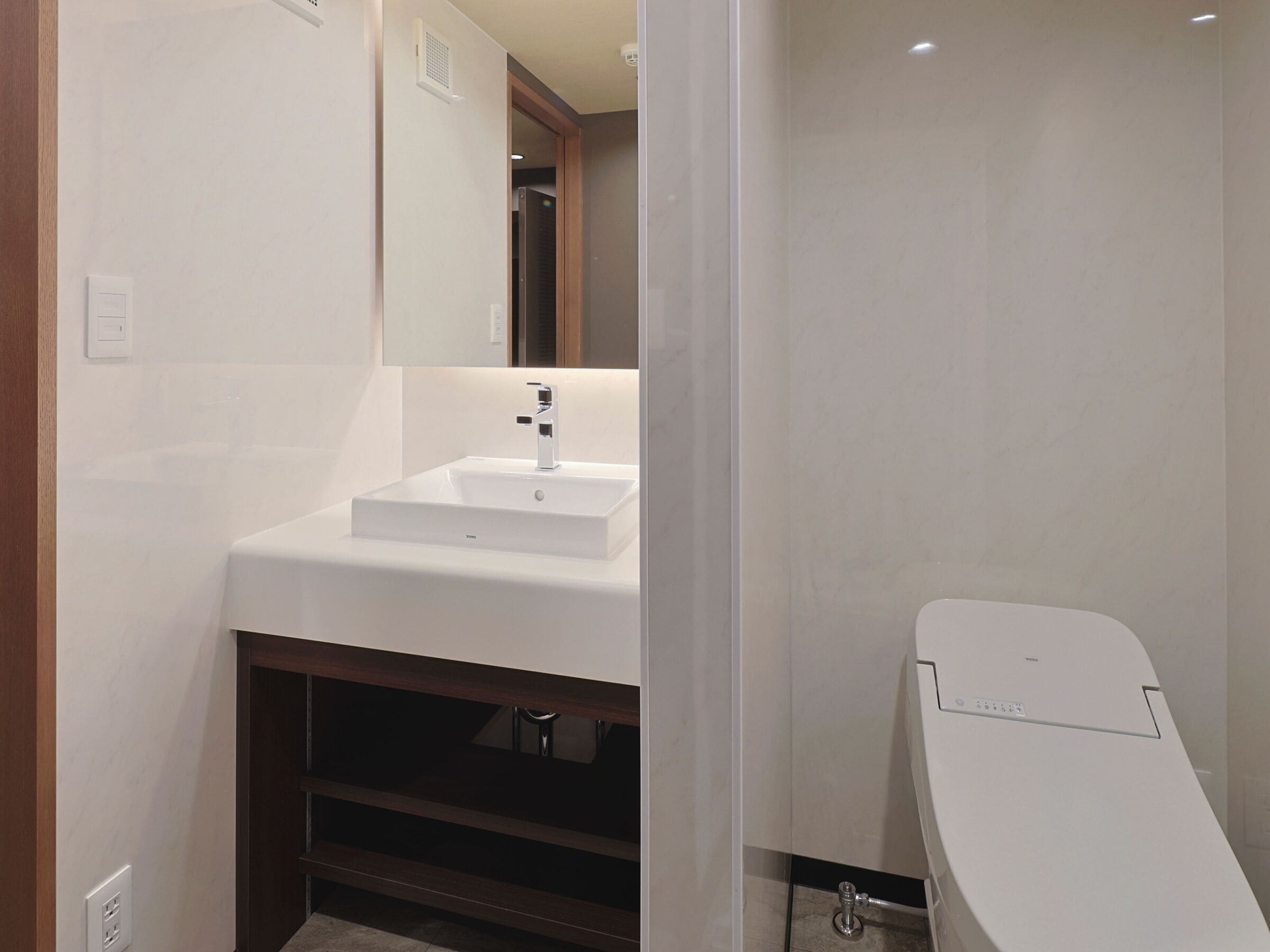 A modern bathroom with a white sink, mirror, and toilet.