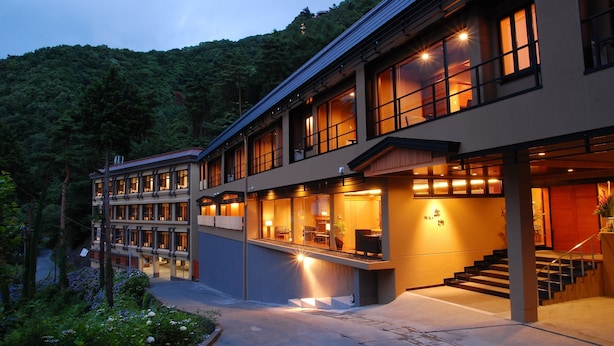 A modern hotel with multiple floors, large windows, and a well-lit entrance. - Rakuyu (Fujikawaguchiko)