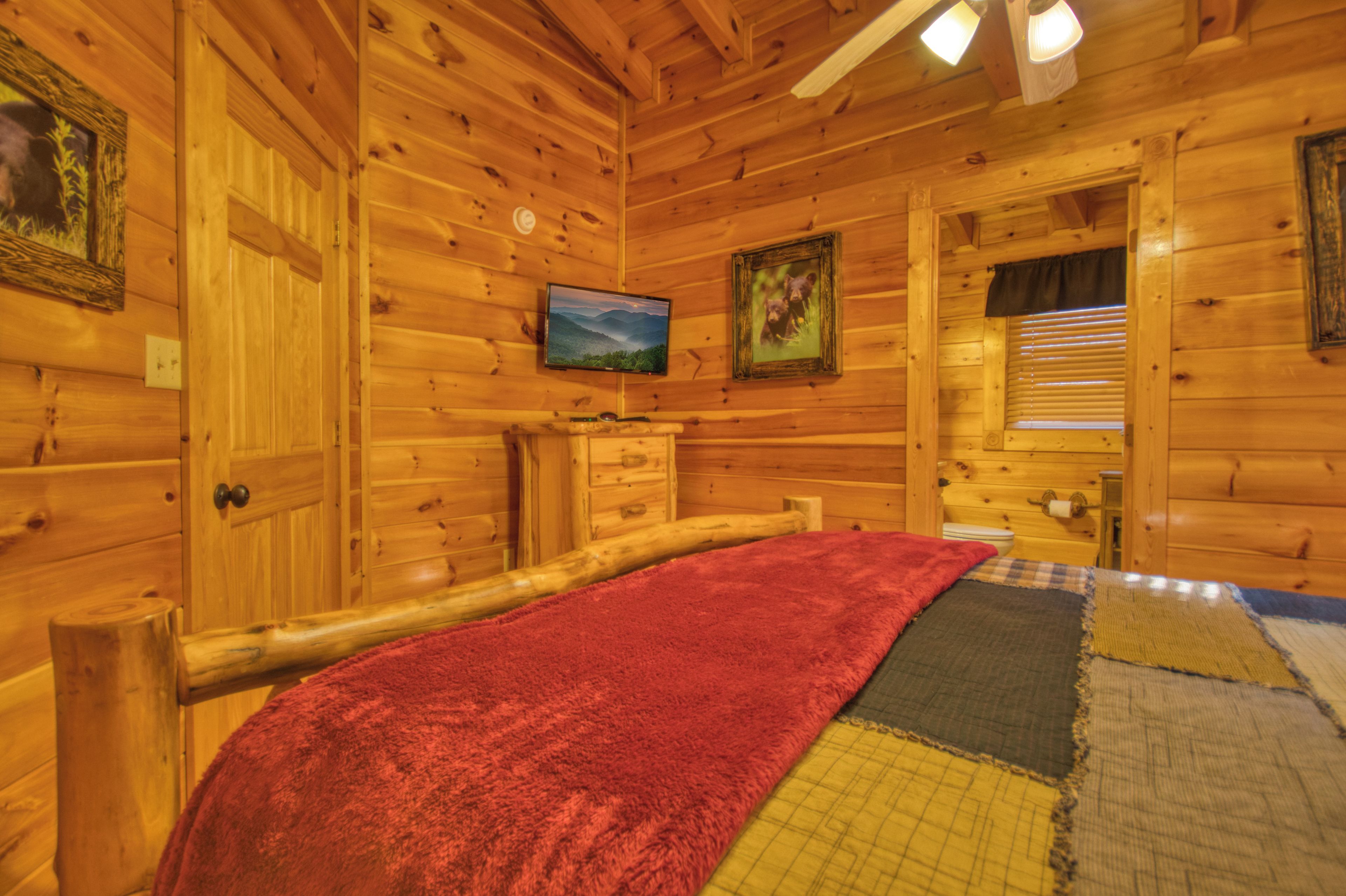 A wooden cabin room with a bed, a television, and a window with blinds.