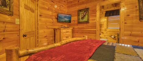 A wooden cabin room with a bed, a television, and a window with blinds.