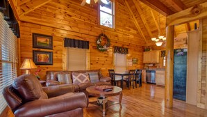 L’intérieur chaleureux d’un chalet avec un plafond en bois, un salon doté d’un canapé en cuir marron, un coin repas et une cuisine avec des meubles en bois et un réfrigérateur.